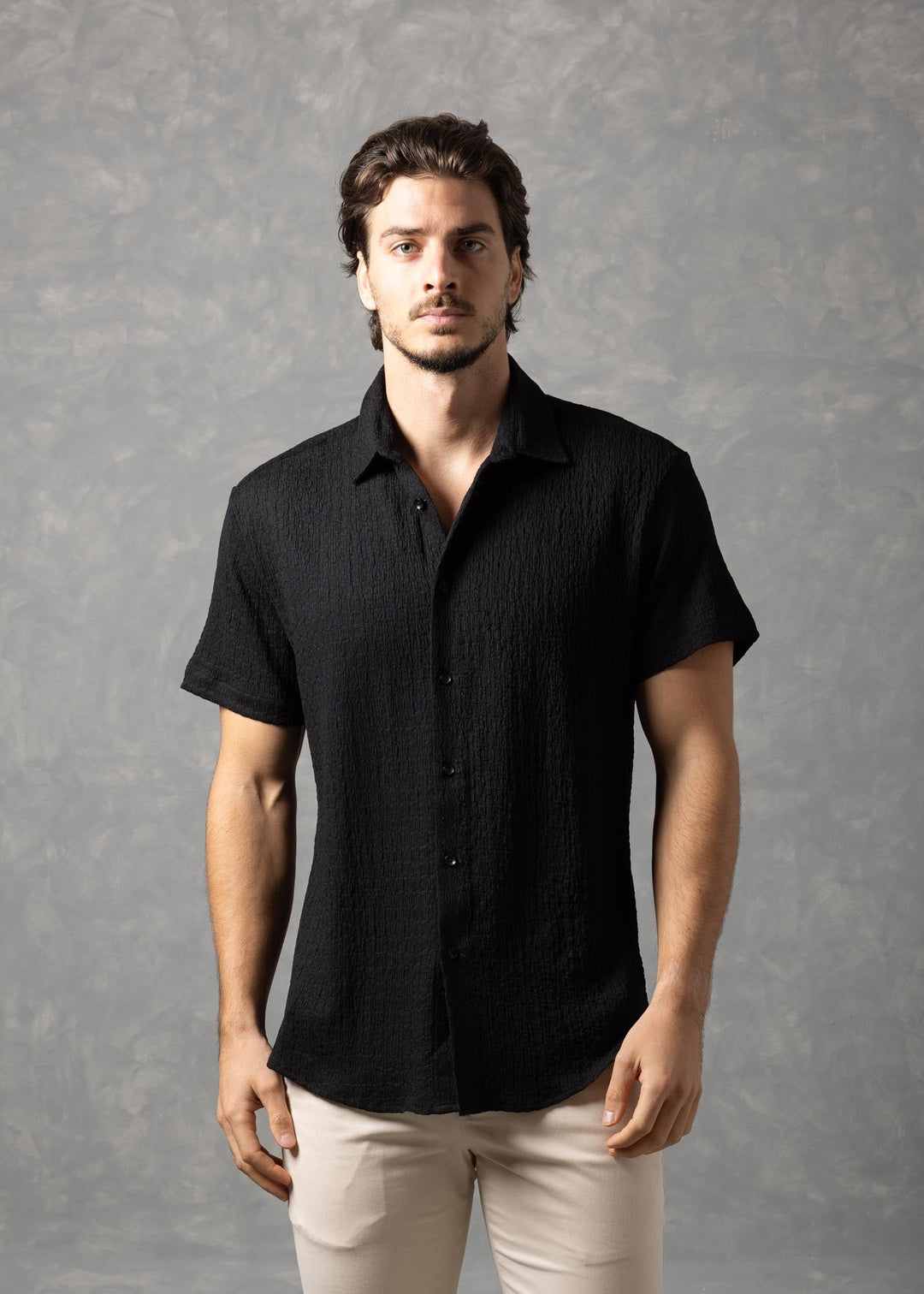 Man wearing a black shirt and beige pants against a gray background