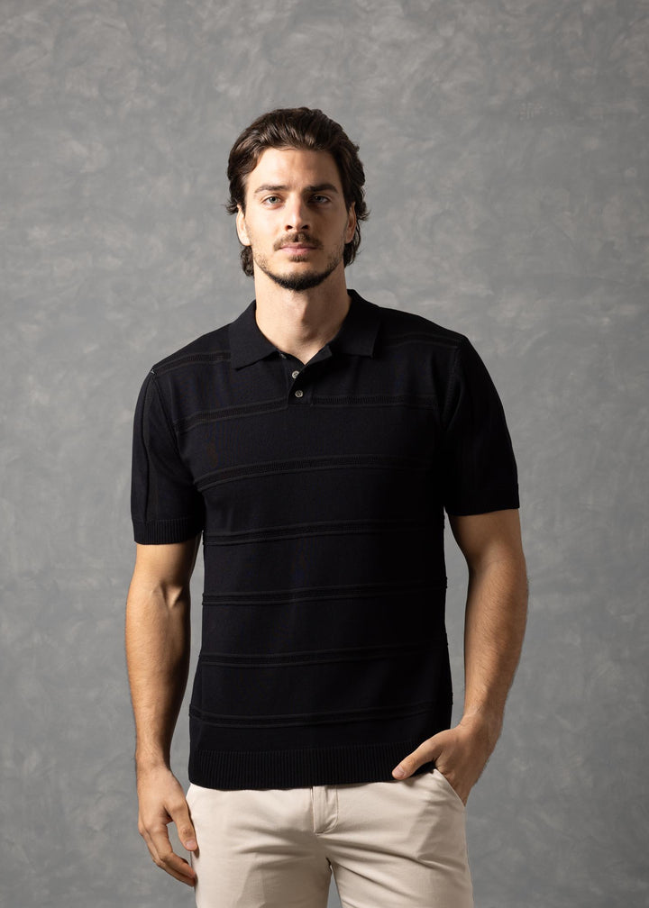 Man wearing a black polo shirt and beige pants against a gray background