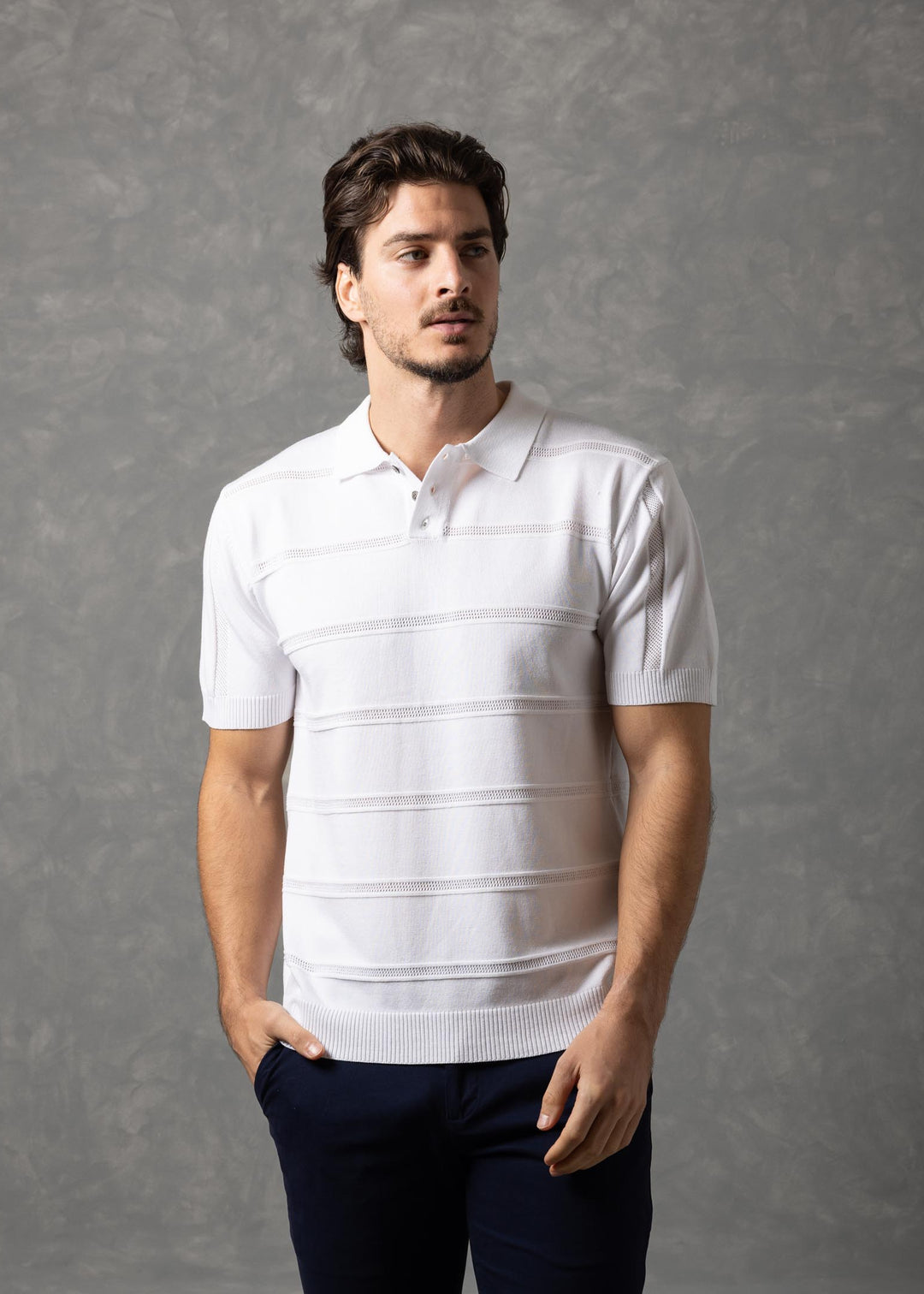 Man wearing a white striped polo shirt and dark pants against a gray background