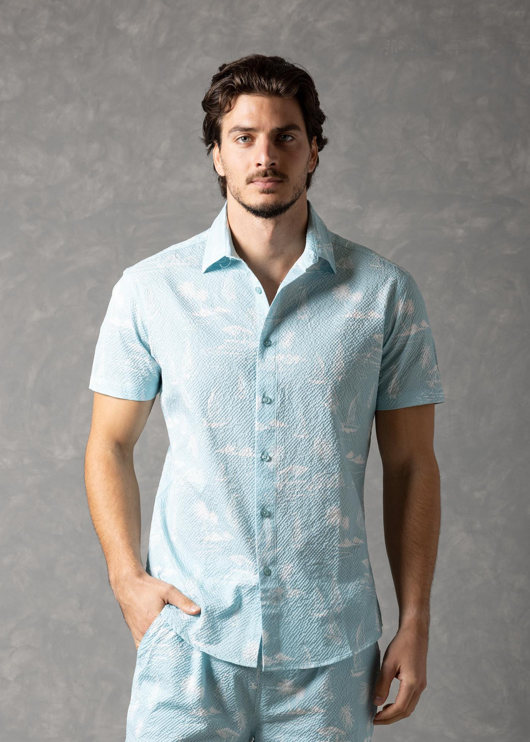 Man wearing a light blue linen shirt and shorts set against a gray background