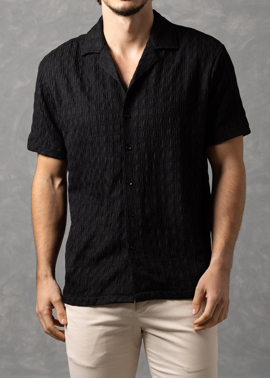 Man wearing a black shirt and beige pants against a gray background