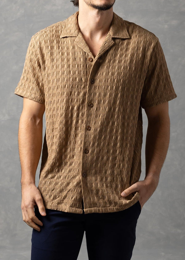 Man wearing a brown textured shirt and dark pants against a gray background