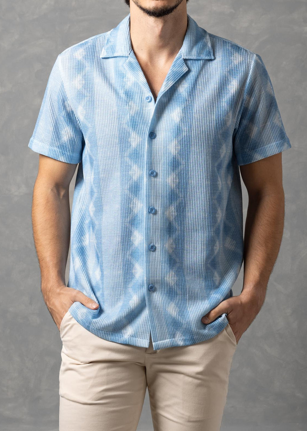 Man wearing a light blue patterned shirt and beige pants against a gray background