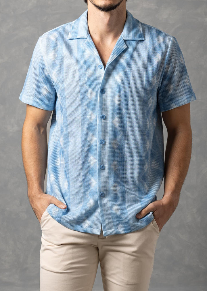 Man wearing a light blue patterned shirt and beige pants against a gray background