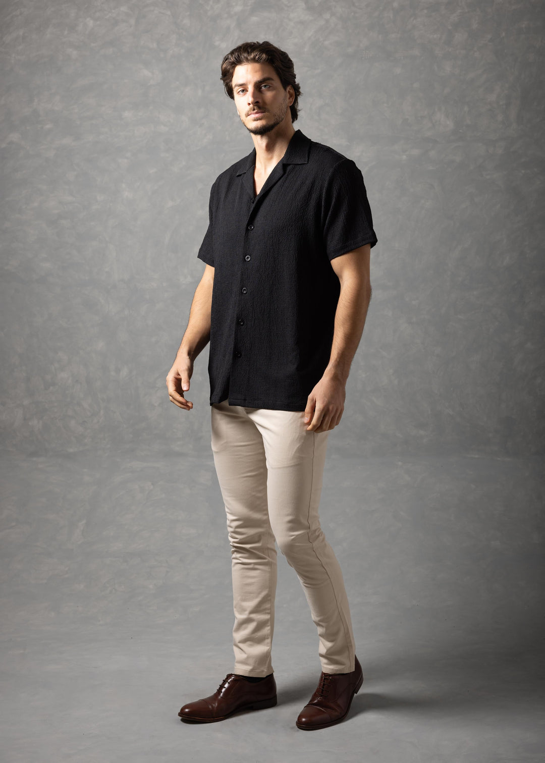 Man wearing a black shirt and beige pants against a gray background