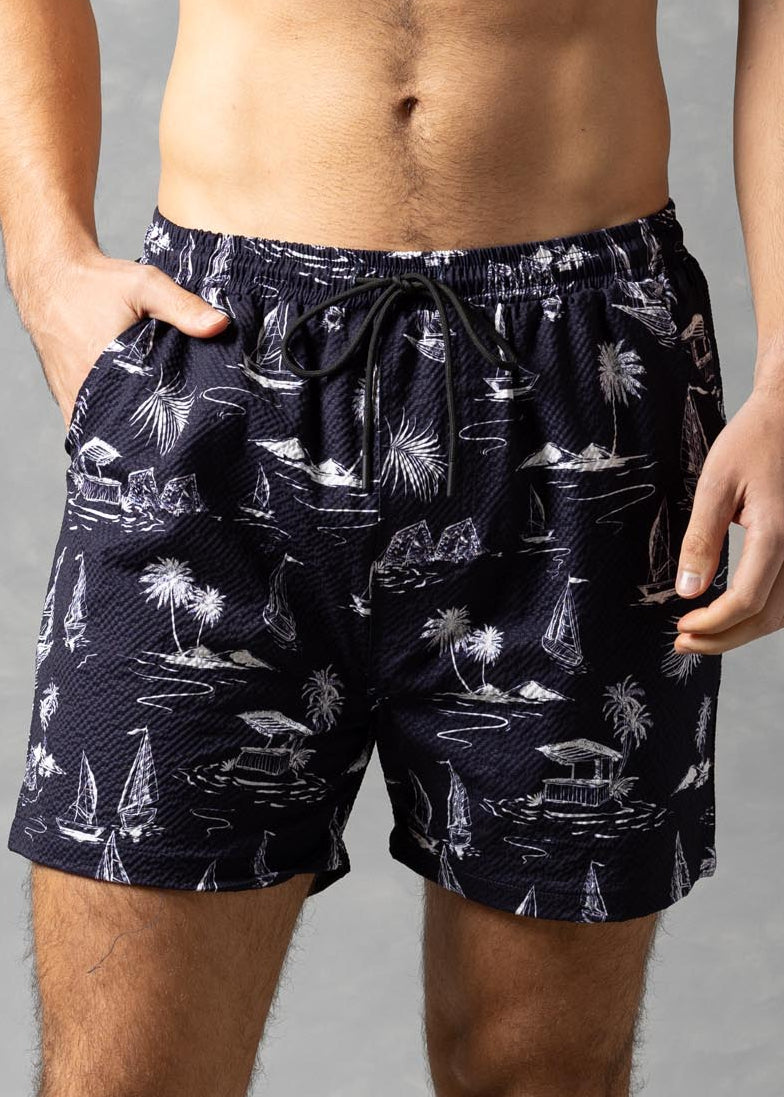 Man wearing navy blue swim shorts with a pattern on a gray background