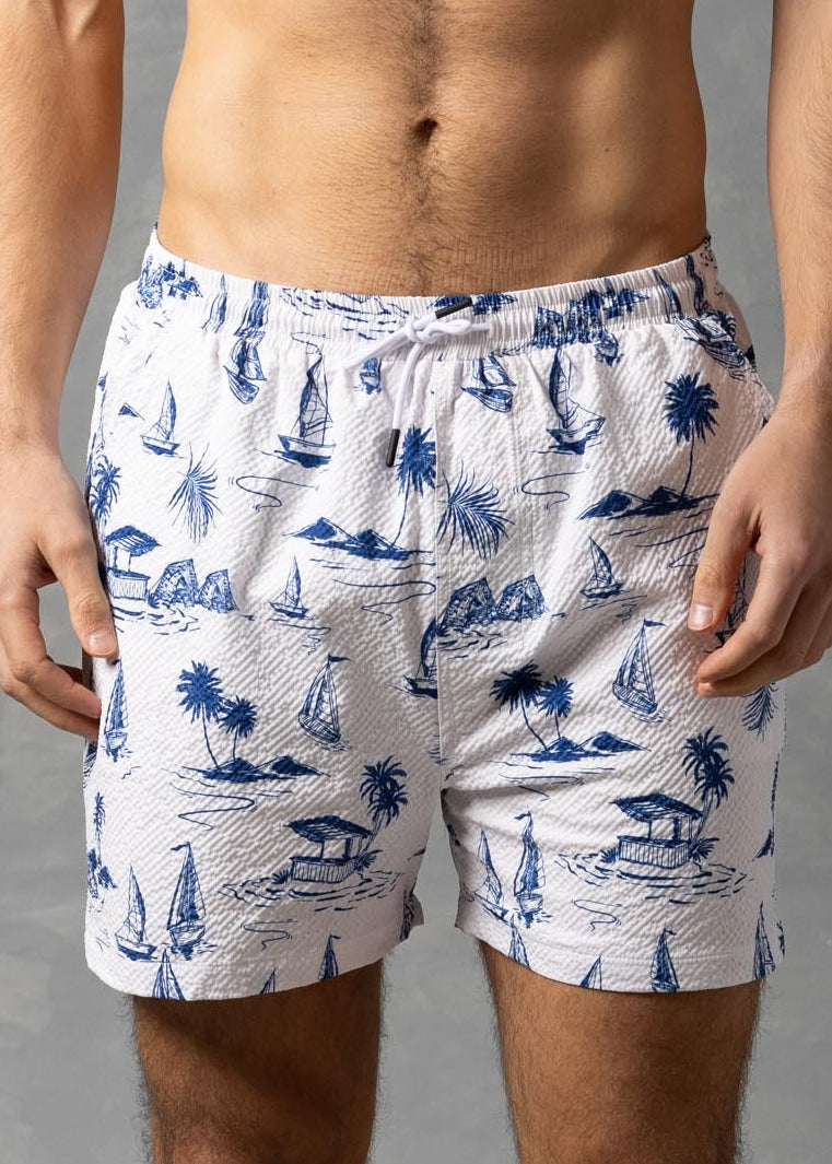 Man wearing white swim shorts with blue patterns against a gray background